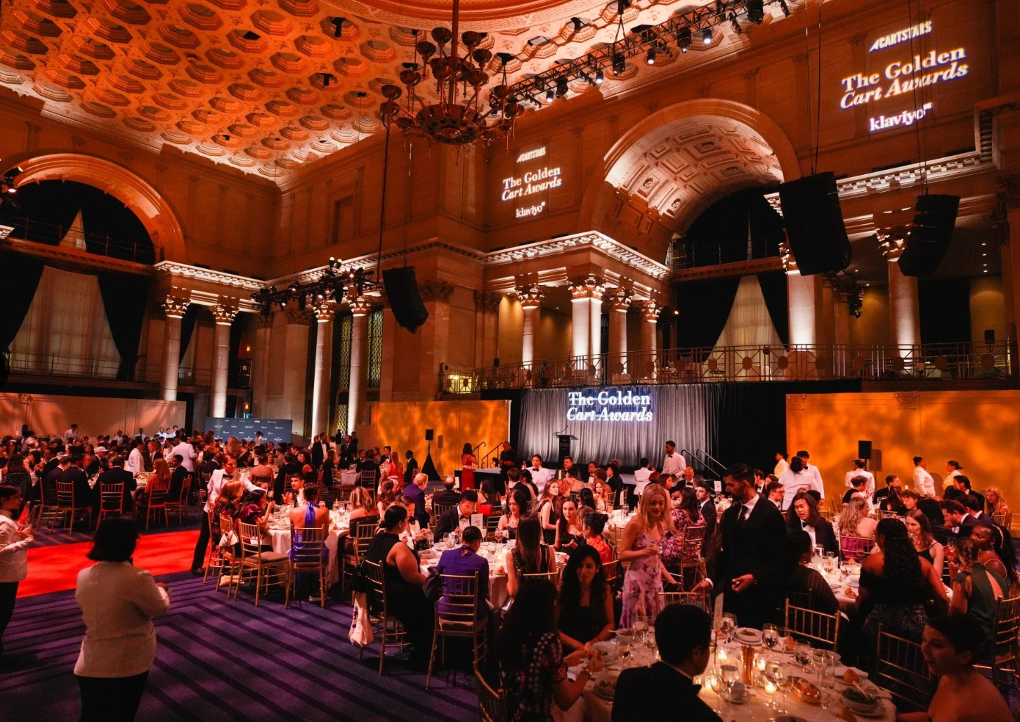 The Golden Cart Awards dinner in the main hall at Cipriani Wall Street, with tables of guests in black tie beneath the coffered ceiling and the event name projected on the walls.